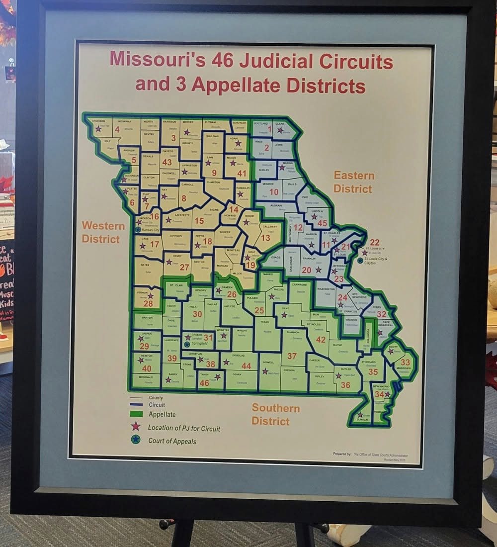 A printed map of Missouri's forty-six judicial circuits in a plain black frame with a pale grey blue mat, standing on an easel.