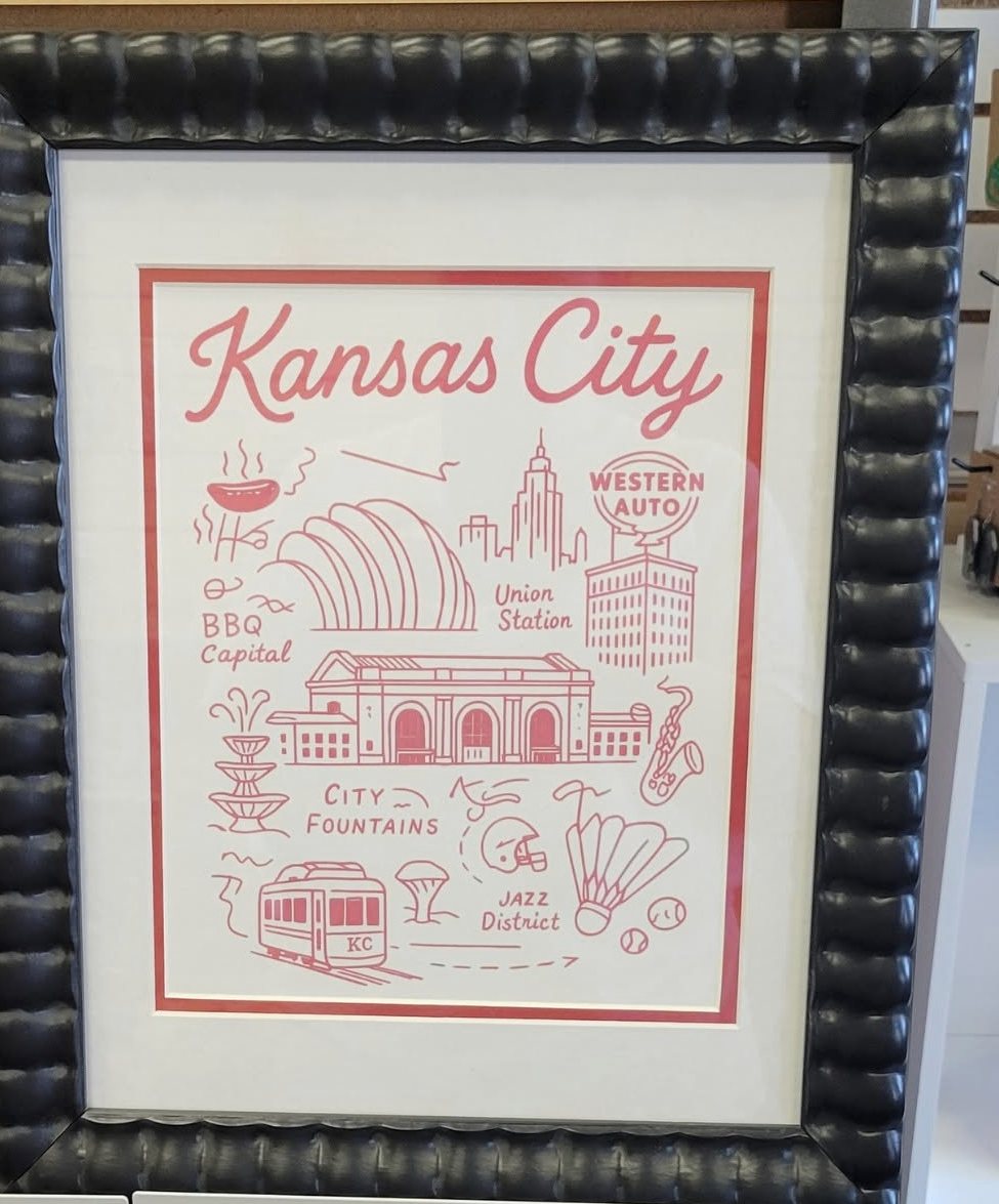 A red and white illustrated Kansas City print in a black beaded wooden frame with a wide white mat.